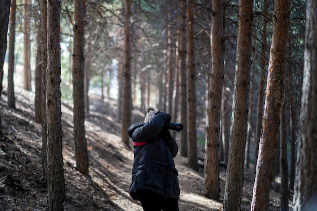 una joven bonita con ropa de abrigo caminando por un bosque tomando fotos