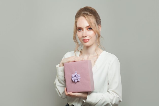 Una joven bonita sosteniendo un regalo rosado sobre un fondo blanco