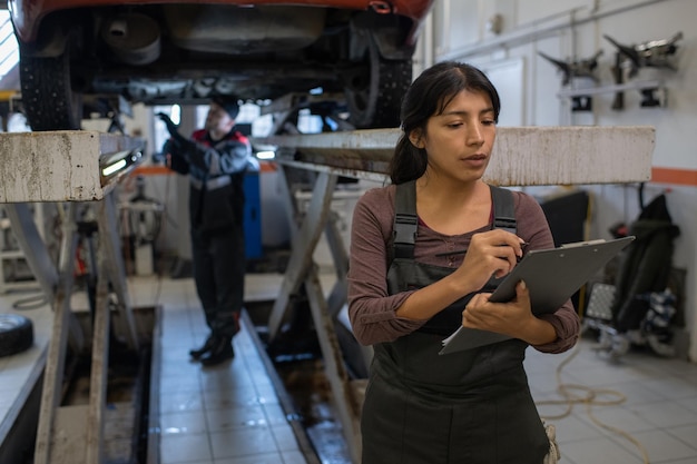 Joven bonita trabajadora del servicio de automóviles haciendo notas