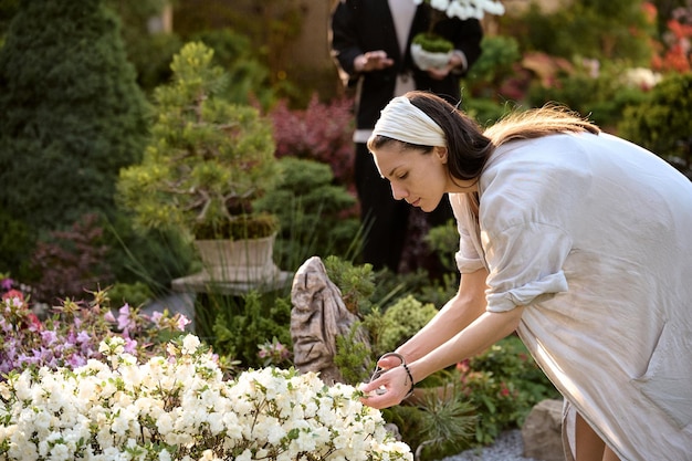 Un joven con un bonsái y una mujer usan tijeras para decorar el arbusto de flores en un jardín de bonsái