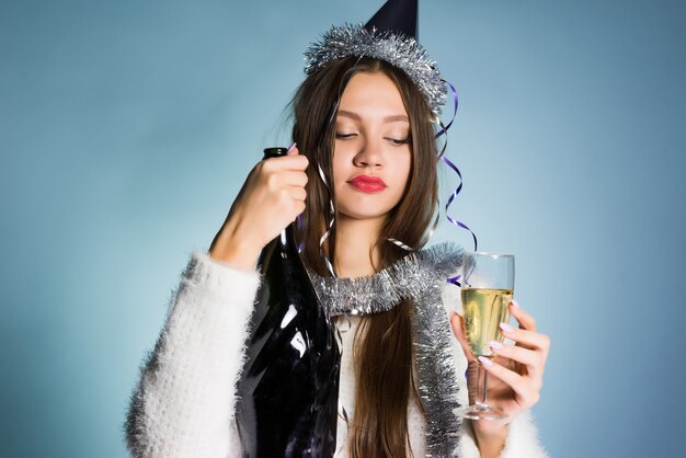 Joven borracha con una gorra en la cabeza celebrando el año nuevo, bebiendo champán