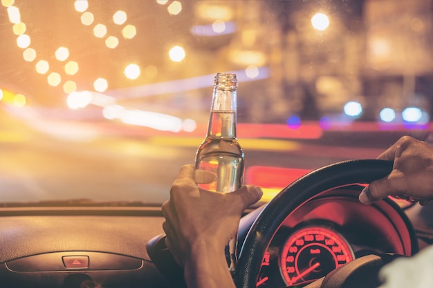 Un joven borracho conduce un automóvil con una botella de cerveza.