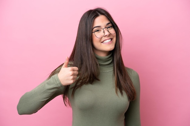 Joven brasileña aislada de fondo rosa con gafas y con el pulgar hacia arriba