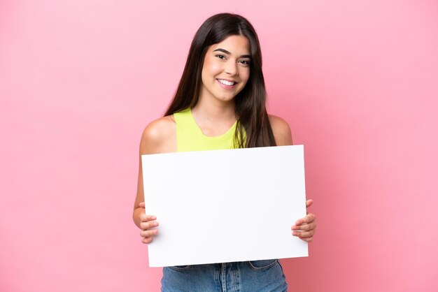 Foto joven brasileña aislada de fondo rosa sosteniendo un cartel vacío con expresión feliz