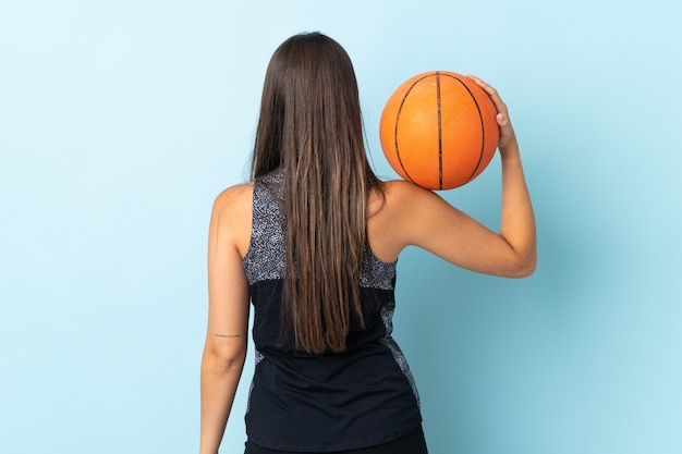 Joven brasileña aislada en la pared azul jugando baloncesto en posición trasera