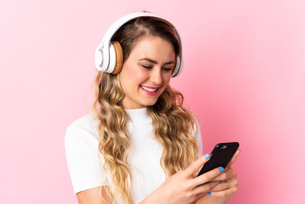 Joven brasileña aislada en rosa escuchando música y mirando al móvil