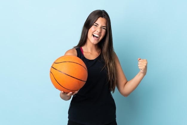 Joven brasileña aislada sobre fondo azul jugando baloncesto