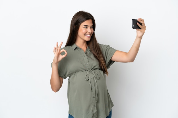 Joven brasileña aislada sobre fondo blanco embarazada y haciendo un selfie