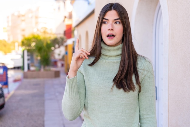 Joven brasileña al aire libre pensando en una idea apuntando con el dedo hacia arriba