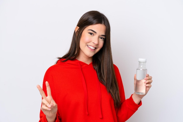 Joven brasileña con una botella de agua aislada de fondo blanco sonriendo y mostrando el signo de la victoria