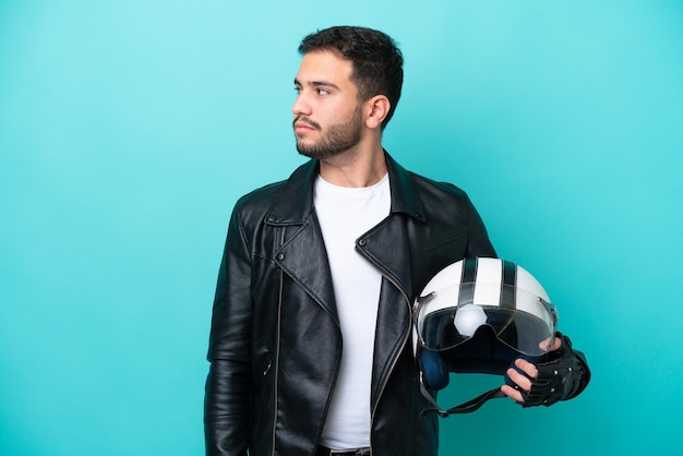 Joven brasileña con casco de motocicleta aislado de fondo azul mirando hacia un lado