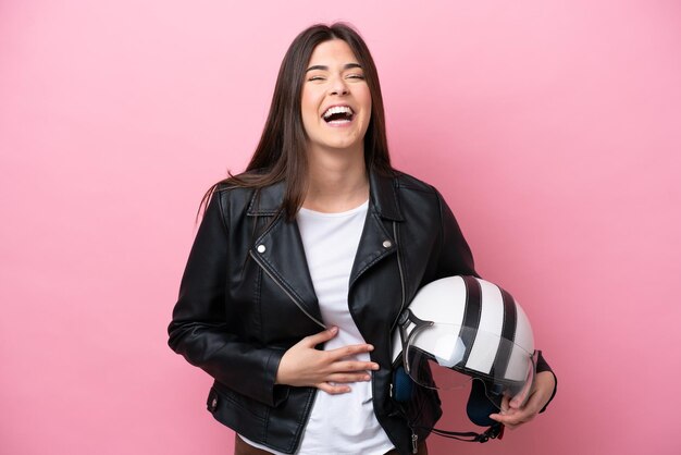 Joven brasileña con un casco de motocicleta aislado de fondo rosa sonriendo mucho