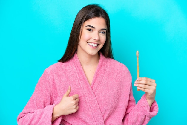 Joven brasileña cepillando dientes aislada de fondo azul con los pulgares hacia arriba porque algo bueno ha sucedido