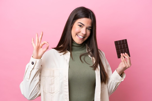 Joven brasileña con chocolat aislado sobre fondo rosa mostrando signo ok con los dedos