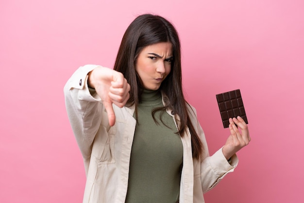 Joven brasileña con chocolate aislado de fondo rosa mostrando el pulgar hacia abajo con expresión negativa