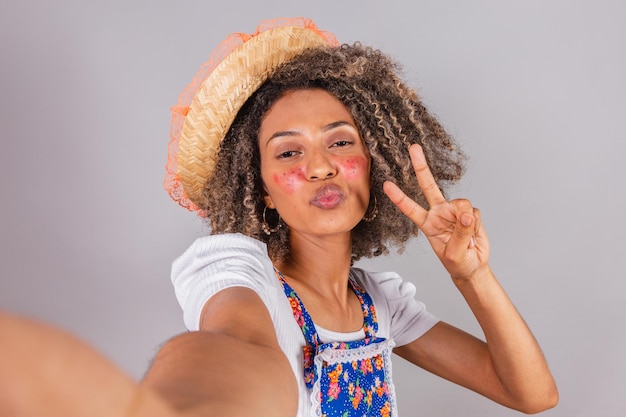 Joven brasileña negra con ropa de campo vestida para el festival Festa Junina Saint John's posar para selfie con smartphone