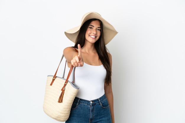 Joven brasileña con Pamela sosteniendo una bolsa de playa aislada sobre fondo blanco mostrando y levantando un dedo