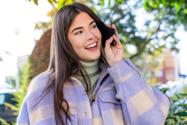 Joven brasileña en un parque manteniendo una conversación con el teléfono móvil