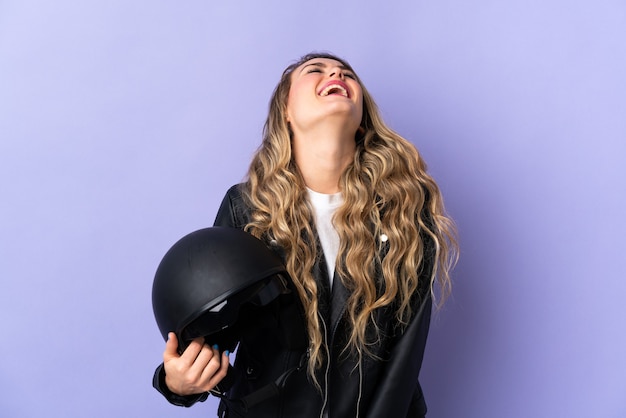 Joven brasileña sosteniendo un casco de motocicleta aislado en púrpura riendo