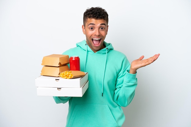 Joven brasileña sosteniendo comida rápida aislada de fondo blanco con expresión facial sorprendida