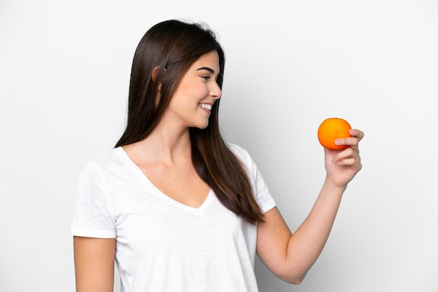 Joven brasileña sosteniendo una naranja aislada de fondo blanco con expresión feliz