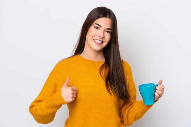 Joven brasileña sosteniendo una taza de café aislada de fondo blanco con los pulgares hacia arriba porque algo bueno sucedió