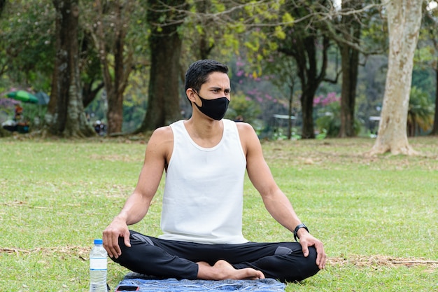 Joven brasileño de 28 años, profesor de yoga, sentado en el césped junto a una botella de agua (vista frontal).