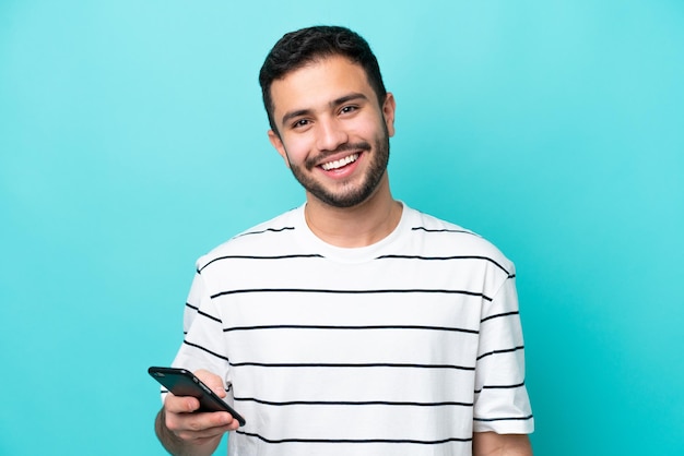 Joven brasileño aislado de fondo azul a través de teléfono móvil