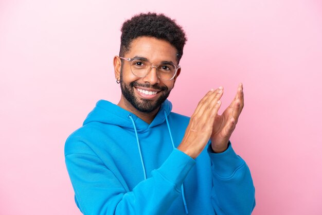 Joven brasileño aislado de fondo rosa con gafas y aplaudiendo