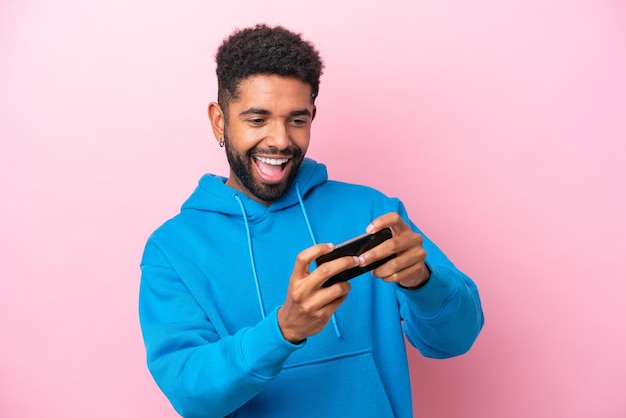 Joven brasileño aislado de fondo rosa jugando con el teléfono móvil