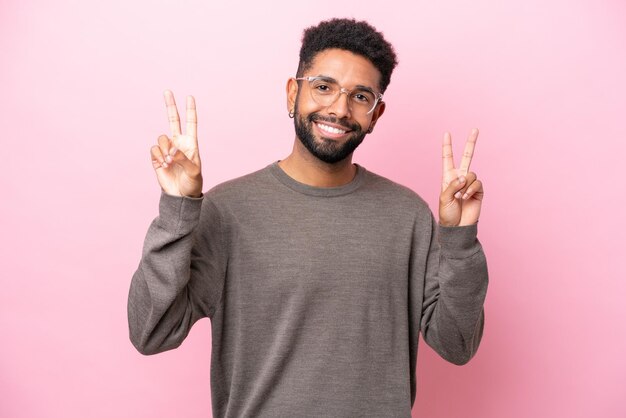 Joven brasileño aislado de fondo rosa que muestra el signo de la victoria con ambas manos