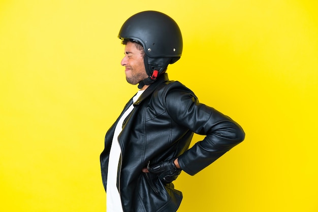 Foto joven brasileño con casco de motocicleta aislado de fondo amarillo que sufre de dolor de espalda por haber hecho un esfuerzo