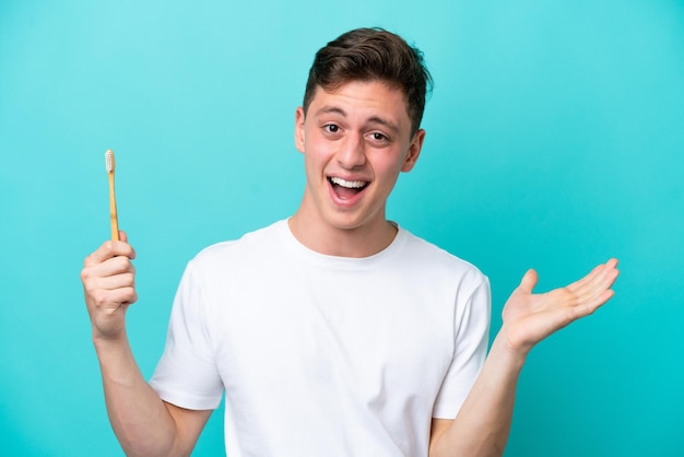 Joven brasileño cepillando dientes aislado de fondo azul con expresión facial conmocionada