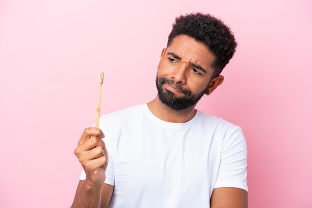 Joven brasileño cepillando dientes aislado de fondo rosa con expresión triste