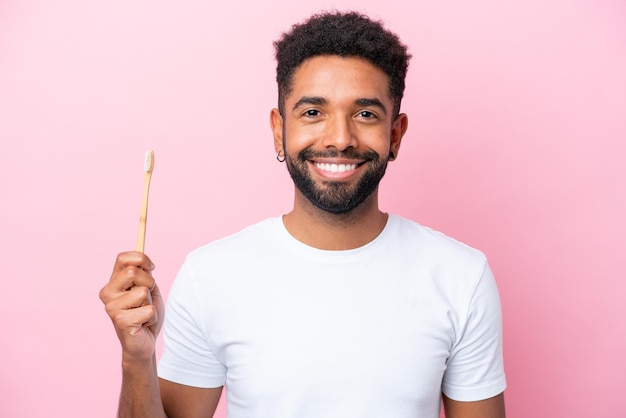 Joven brasileño cepillando dientes aislado de fondo rosa sonriendo mucho