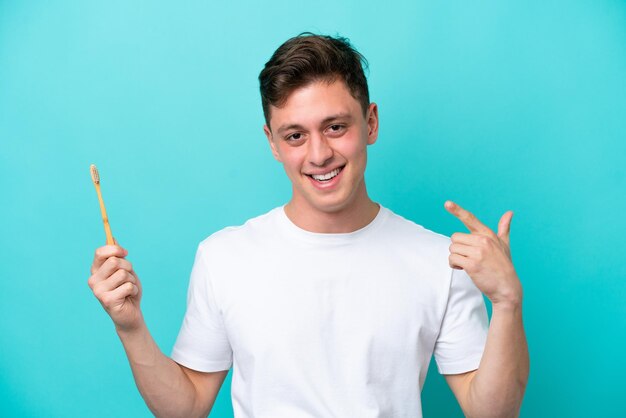 Joven brasileño cepillarse los dientes aislado sobre fondo azul dando un pulgar hacia arriba gesto