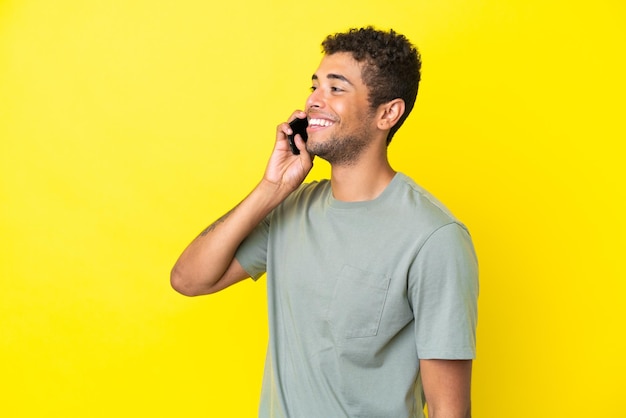 Joven brasileño guapo aislado de fondo amarillo manteniendo una conversación con el teléfono móvil