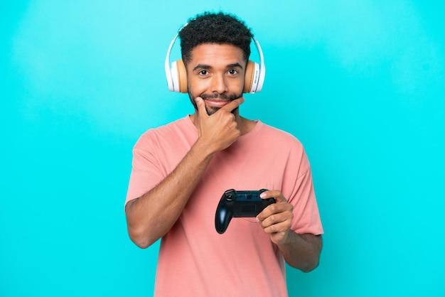 Joven brasileño jugando con un controlador de videojuegos aislado en un pensamiento de fondo azul