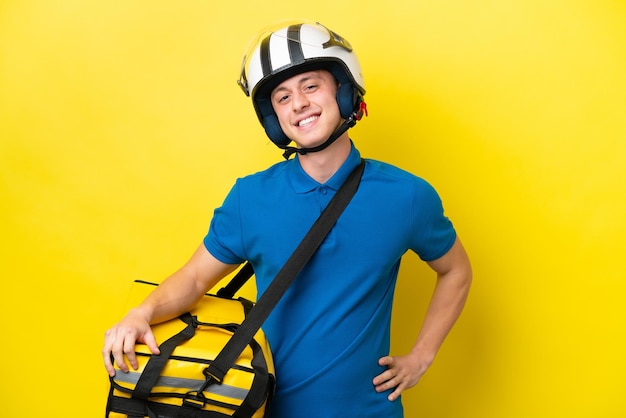 Joven brasileño con mochila térmica aislado de fondo amarillo posando con los brazos en la cadera y sonriendo