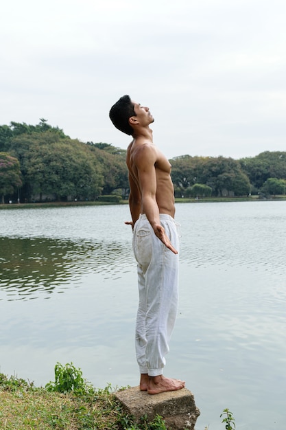 Joven brasileño de pie junto a un lago con los brazos abiertos y mirando hacia arriba.