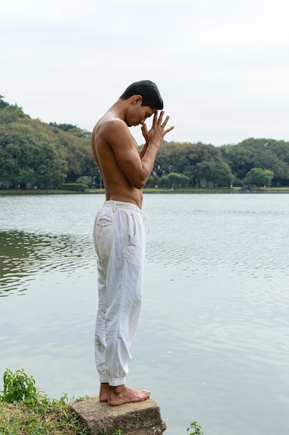 Joven brasileño de pie junto a un lago en una posición agradecida.