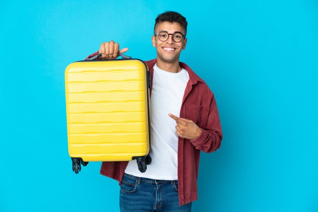 Joven brasileño sobre pared aislada en vacaciones con maleta de viaje