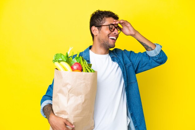 Joven brasileño sosteniendo una bolsa de compras aislada de fondo amarillo sonriendo mucho