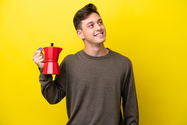 Joven brasileño sosteniendo una cafetera aislada de fondo amarillo pensando en una idea mientras mira hacia arriba