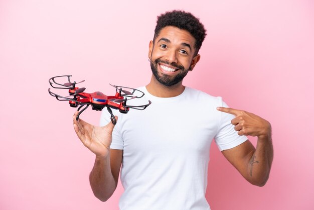 Joven brasileño sosteniendo un dron aislado de fondo rosa con expresión facial sorpresa