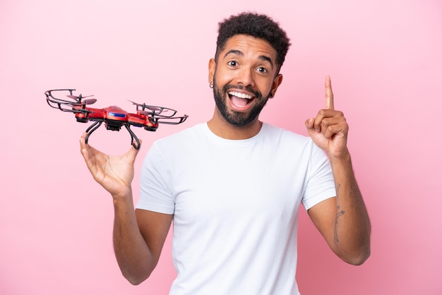 Joven brasileño sosteniendo un dron aislado de fondo rosa señalando una gran idea