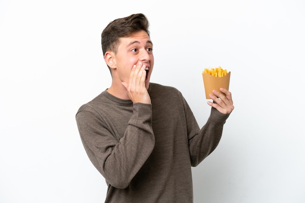 Joven brasileño sosteniendo patatas fritas aisladas de fondo blanco gritando con la boca abierta a un lado