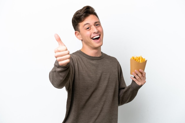 Joven brasileño sosteniendo patatas fritas aisladas de fondo blanco con los pulgares hacia arriba porque algo bueno ha sucedido