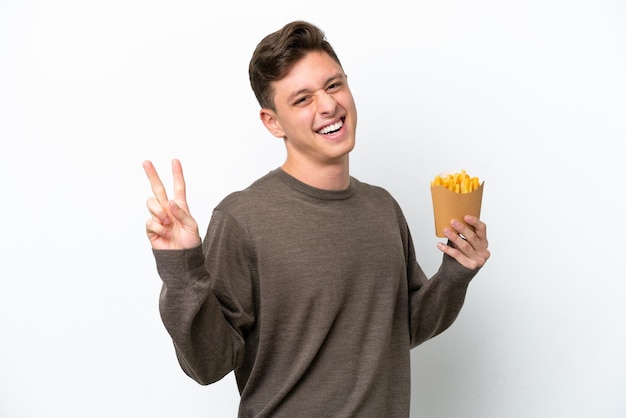 Joven brasileño sosteniendo patatas fritas aisladas de fondo blanco sonriendo y mostrando el signo de la victoria