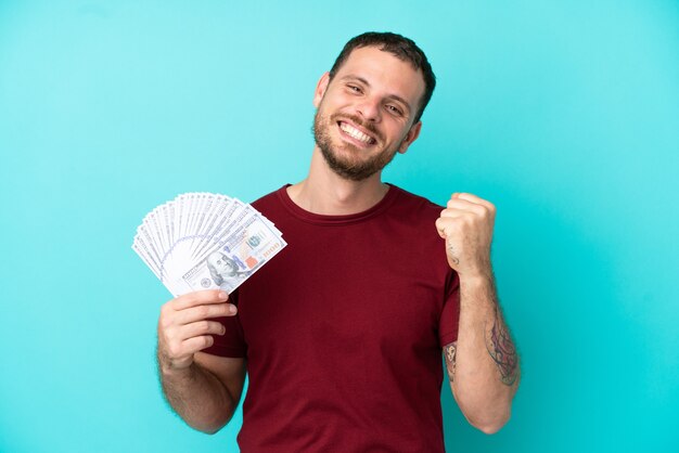 Joven brasileño tomando un montón de dinero sobre antecedentes aislados celebrando una victoria en la posición ganadora